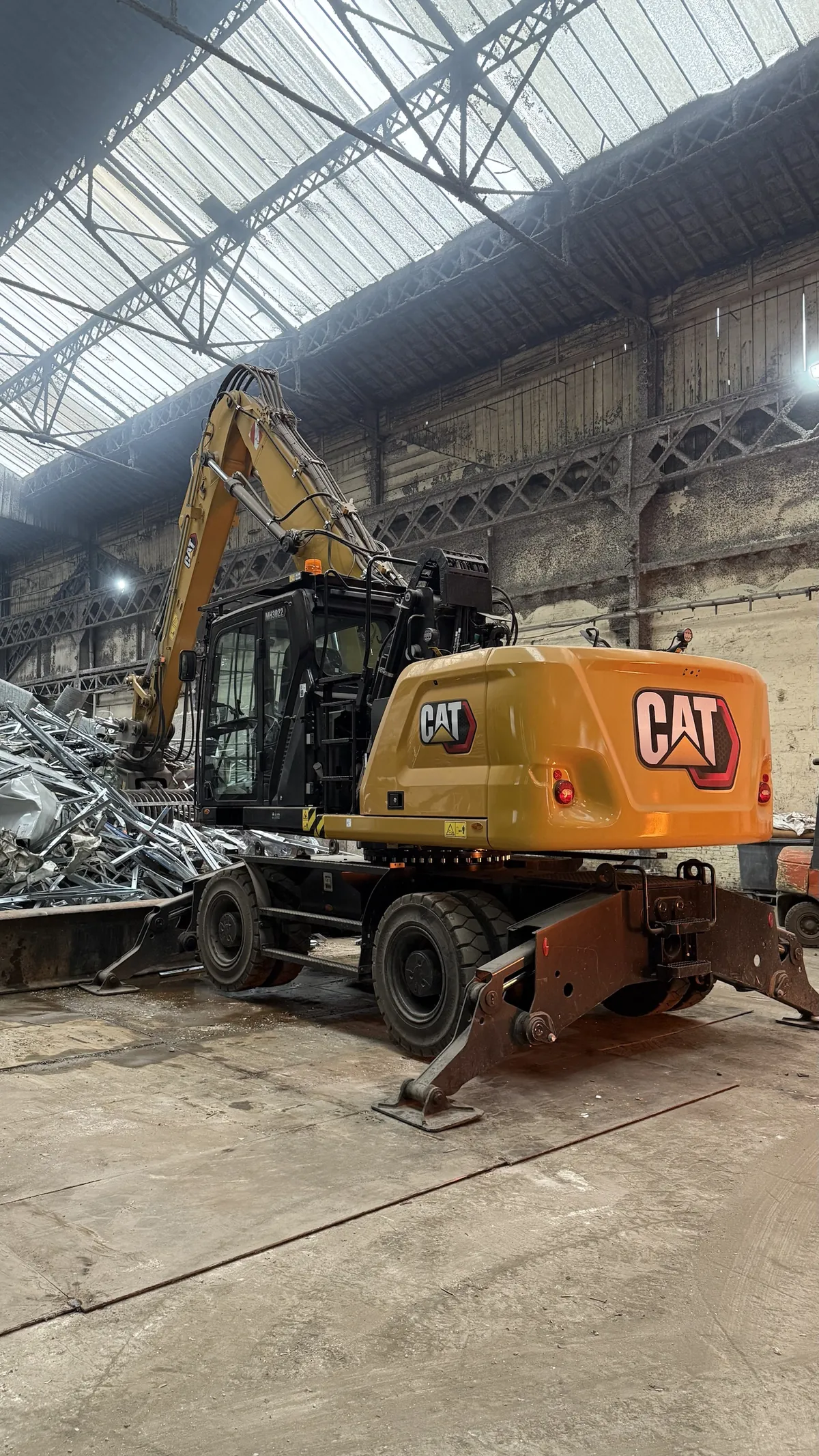 Une pelle CAT jaune à pince de tri, garée devant un tas de ferrailles