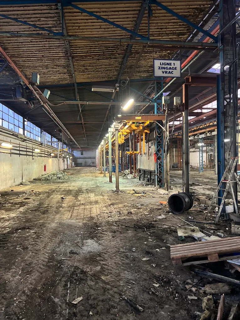 Hall d’usine vidé avant démolition, au-dessus d’une ancienne ligne de zingage